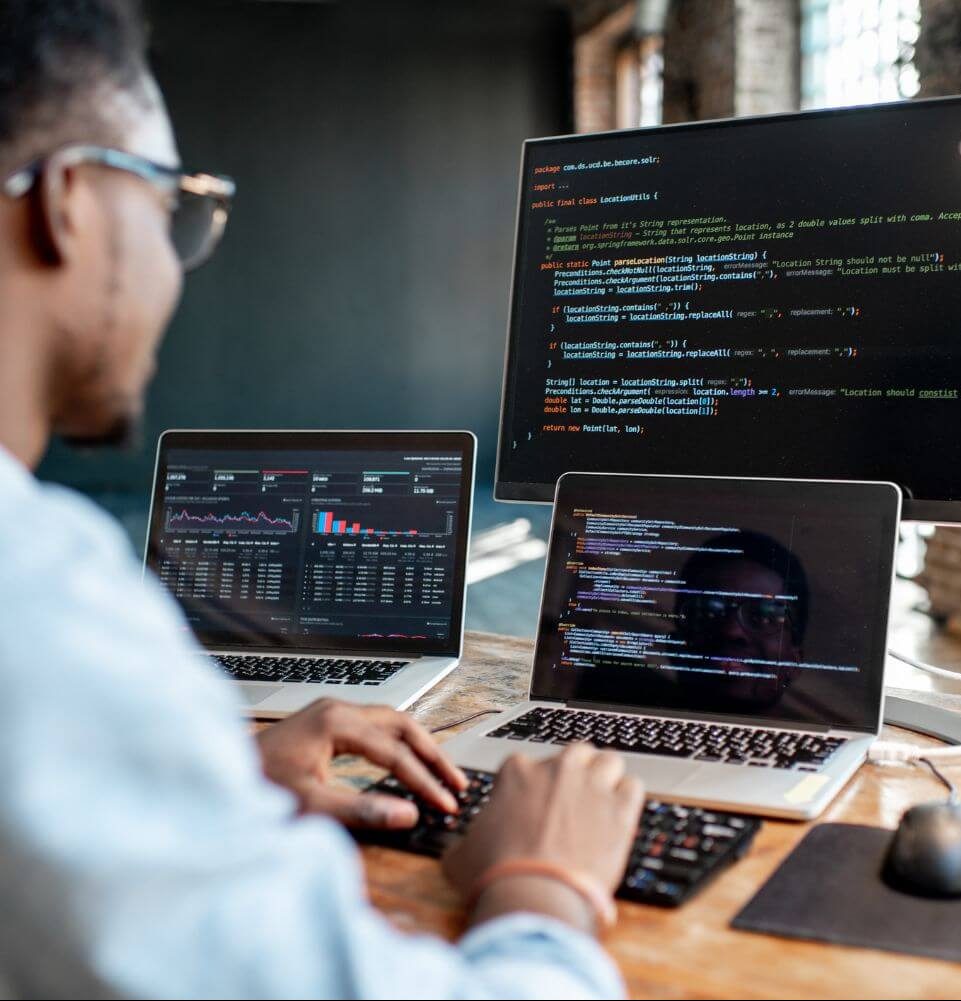 programmer writing program code sitting at the workplace with three monitors